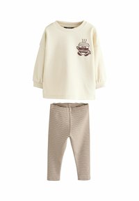 Conjunto para niños que incluye una camiseta de manga larga color crema con un gráfico de una taza de café "Babyccino" y leggings a rayas marrón y blanco.