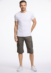 Witte crew-neck t-shirt gecombineerd met olijfgroene cargo shorts met zijzakken, afgewerkt met witte sneakers. De stof lijkt lichtgewicht en casual.
