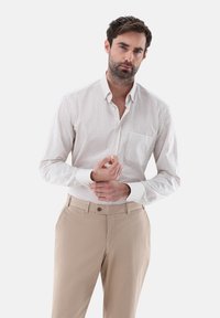 Helles karierter Hemd mit Button-Down-Kragen und einer Brusttasche, kombiniert mit beigen Hosen. Schlichtes, tailliertes Design.