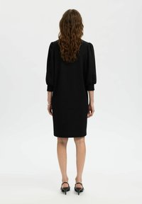 Mustalükk, millega on sobiv siluett, puffseened varrukad ja põlvepikkune ääreosa. Sile tekstuur. Kandmiseks mustade kontsakingadega, näidates jalgu.