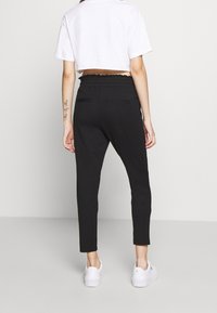 Svarta joggers med elastisk midja, avsmalnande ben, två bakfickor och mjukt material, tillsammans med en vit kortärmad t-shirt och vita sneakers.