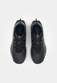 Baskets de sport noires avec tige en mesh, accents texturés, bout rond et semelle grise contrastante. Lacets et petite languette à l'arrière.