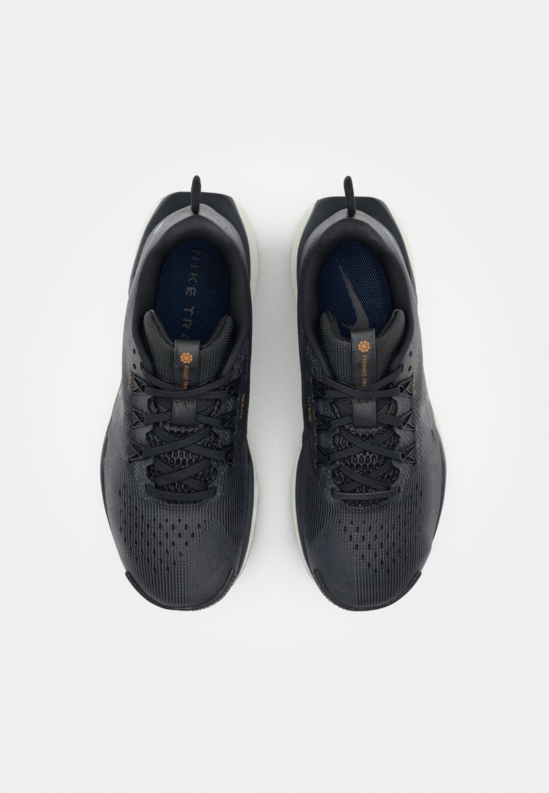 Zapatillas deportivas negras con parte superior de malla, acentos texturizados, puntera redondeada y suela gris en contraste. Cierre de cordones y pequeña lengüeta en el talón.