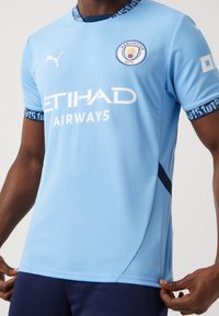 Vaaleansininen lyhythihainen jalkapallopaita tummansinisillä yksityiskohdilla, jossa on pyöreä kaulus, Manchester Cityn logo ja ETIHAD AIRWAYS -brändäys.