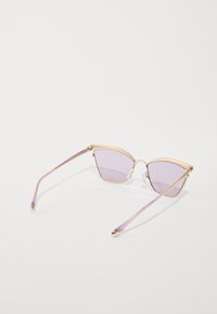 Sunglasses s mačkama u obliku oka sa zlatnim metalnim okvirom, svijetloplavim staklima i prozirnim ljubičastim vrhovima. Ima male zlatne akcentne detalje na drškama.