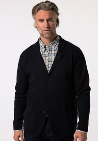 Tmavě modrý cardigan z pleteniny, s klopovým límcem, dvěma předními kapsami a třemi knoflíky, položený přes kostičkovanou košili.