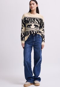 Maglione lavorato a maglia con motivi animali crema e neri, abbinato a jeans dark blue a gamba larga. Il modello indossa calzature beige foderate in pile.