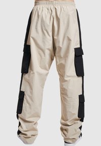 Beige cargobroeken met zwarte zijpanelen, een elastische tailleband, meerdere zijzakken en een relaxte pasvorm. Gemaakt van lichtgewicht stof.