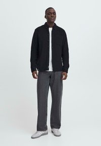 Black button-up shirt over a white t-shirt, paired with gray patterned wide-leg pants and gray sneakers. Minimalistic design and muted colors.