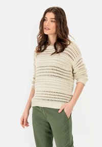 Beige gebreide trui met open weefpatroon en geribde manchetten, gecombineerd met olijfgroene broek. Casual pasvorm met ronde halslijn.