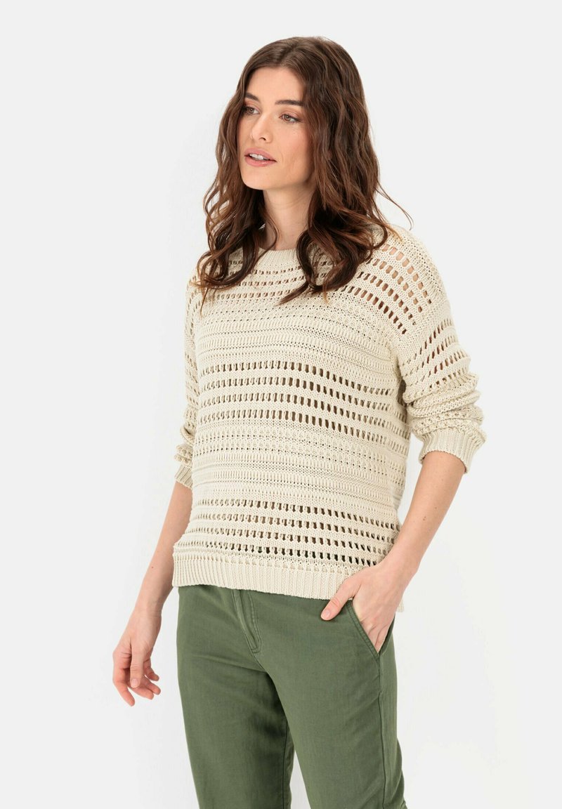 Beżowy sweter dziany z otwartym splotem i ściągaczami na rękawach, w zestawieniu z oliwkowymi spodniami. Luźny krój z okrągłym dekoltem.