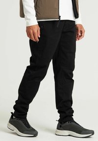Pantalones negros ajustados con un corte entallado, que cuentan con bolsillos tipo cargo y un acabado mate. Acompañados de zapatillas deportivas grises con contraste de textura.