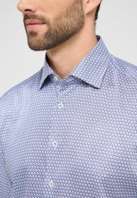 Lichtblauw gekleed shirt in een katoenmix, met een herhalend druppelontwerp in donkerblauw. Klassieke kraag en opvallende knoopdetails.