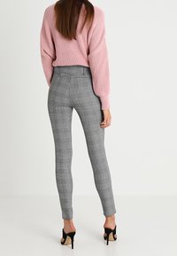 Grijze geruite broeken met een slim fit, hoge taille en enkel-lang ontwerp. Gepaard met een roze gebreide trui en zwarte hakken.