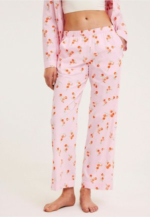 Lichtroze pyjamabroek met elastische taille en oranje fruitpatroon, gedragen met bijpassende top met lange mouwen en witte cropped tanktop.