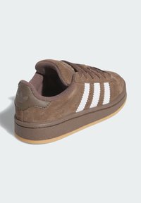 Brown suede sneakers with white three-stripe design, rubber sole, flat laces, padded collar, and textured detailing near the heel.