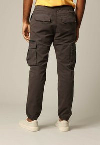 Cargo broek in donkergrijze stof met elastische manchetten, zij- en achterzakken, en een relaxte pasvorm, gedragen met witte sneakers.