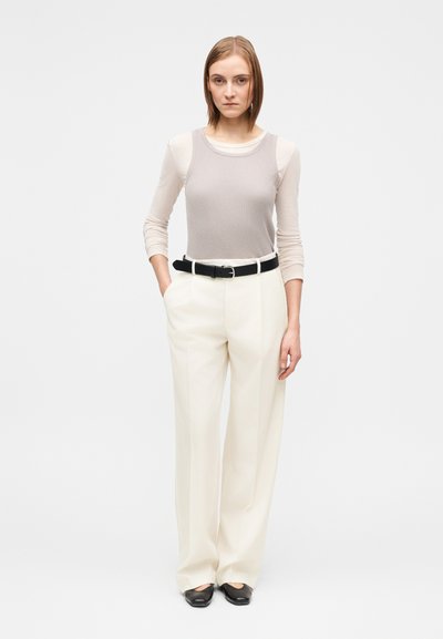 Šviesiai pilkas ribuotas tankinis viršus, dėvimas ant smėlio spalvos ilgomis rankovėmis viršaus, derinamas su kreminės spalvos platėjusių kelnių ir juodu diržu. Juodi batai.