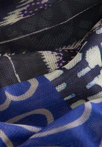 Textile avec un motif bleu, noir et crème clair, tissu texturé avec des designs tissés, couches superposées et détails complexes.