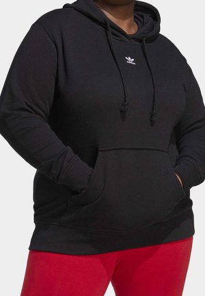 Sort hættetrøje lavet af blødt stof med en kængurulomme, justerbare snore og et hvidt logo på brystet. Røde leggings er synlige.