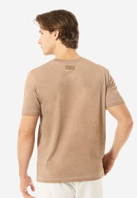 Beige T-Shirt mit kurzen Ärmeln aus weichem Stoff. Es hat einen runden Ausschnitt, ein Etikett auf der Rückseite und eine glatte, gleichmäßige Textur.