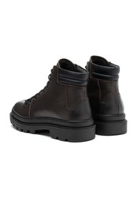 Brązowe skórzane buty z wysoką cholewką, czarnymi akcentami, teksturowanym wykończeniem i bieżnikiem, z sześcioma metalowymi oczkami na sznurówki.