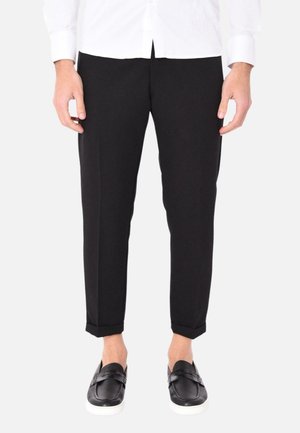 Pantaloni neri a vestibilità slim, realizzati in tessuto morbido, con orlo arrotolato. Indossati con mocassini neri su uno sfondo bianco.