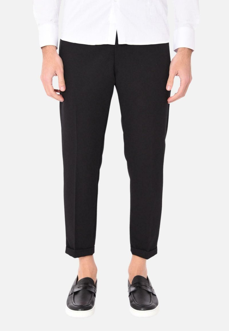 Pantaloni neri a vestibilità slim, realizzati in tessuto morbido, con orlo arrotolato. Indossati con mocassini neri su uno sfondo bianco.