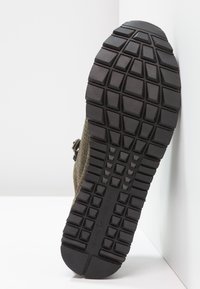 Scarpa verde oliva con parte superiore in mesh traspirante e suola in gomma nera. Il motivo del battistrada presenta scanalature profonde per una migliore aderenza. Dettaglio della fascia regolabile.