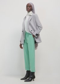 Blazer gris clair à double boutonnage, associé à un chemisier blanc et un pantalon vert menthe. Bottines noires complètent la tenue.
