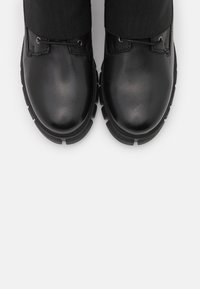 Bottes en cuir noir avec bouts arrondis, dessus texturé et semelles en caoutchouc. Dotées de lacets et d'œillets pour un maintien sécurisé.