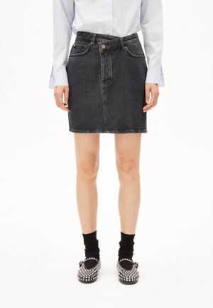 Jupe crayon en denim foncé avec une taille cintrée, des poches avant et des coutures contrastées, assortie à des chaussettes noires et des chaussures ornées.