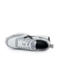 Zapatilla deportiva gris con cordones blancos, material de ante y malla, suela gruesa, acentos negros y una tira negra para tirar.