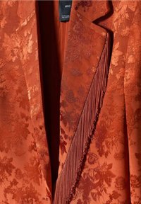 Rustiikkinen teksturoitu bleiseri, jossa kukkakuvioinen kohokuviointi, hapsureunukset ja sileä satiinimainen viimeistely.