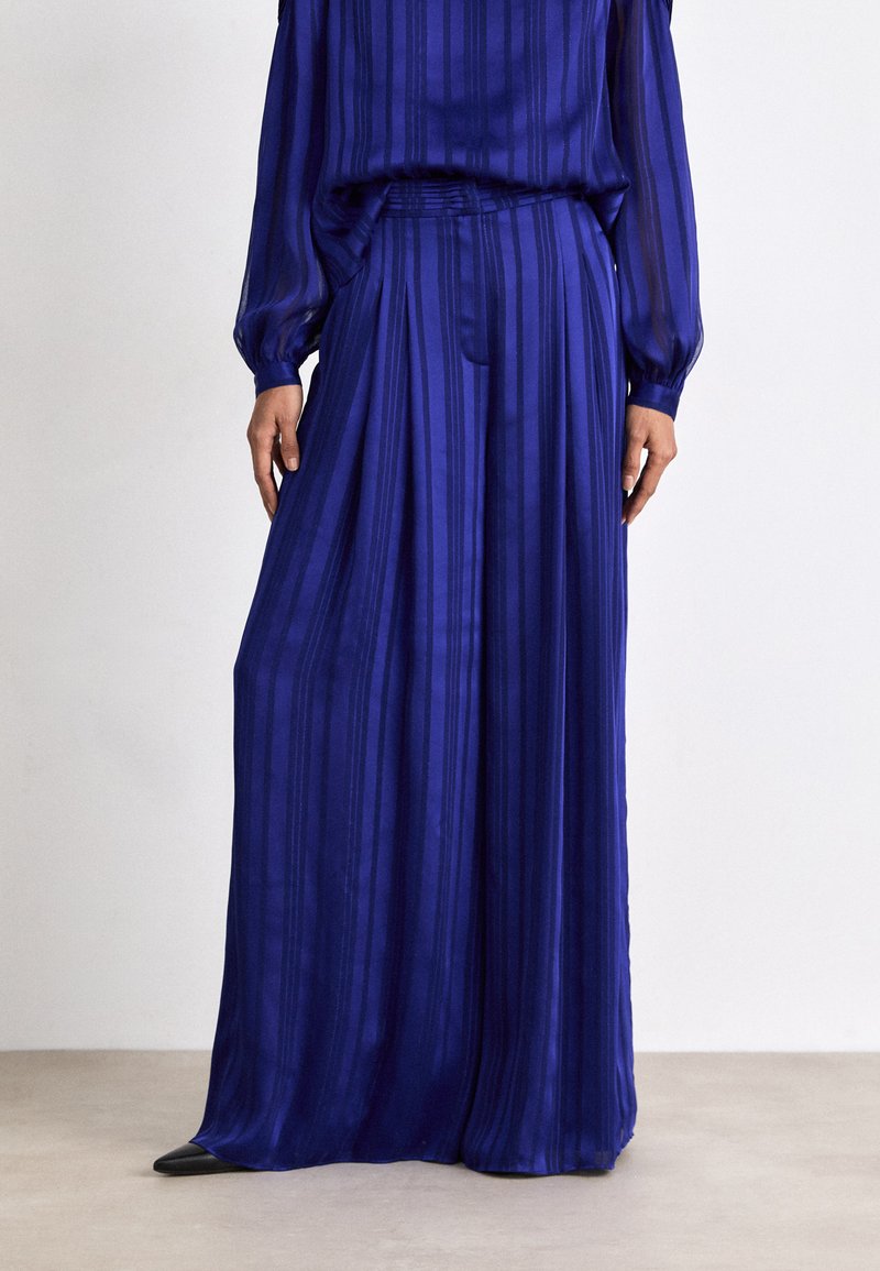 Pantalons longs plissés en tissu bleu vif avec des rayures verticales. Dotés d'une taille élastique et assortis d'un haut coordonné.