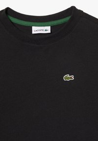 T-shirt di cotone nero con collo rotondo, dotata di un interno del collo verde e di un piccolo logo ricamato a forma di coccodrillo verde sul petto.