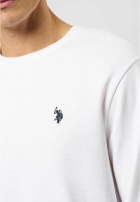 Witte katoenen crewneck sweatshirt met een klein donkerv blauw geborduurd logo op de linkerborst, met een gladde textuur en een casual pasvorm.