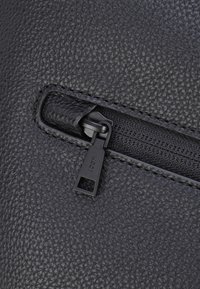 Materiale in pelle nera testurizzata con una tasca con zip. La zip è dotata di un piccolo tirante rettangolare, impresso con il marchio "JOOP!".