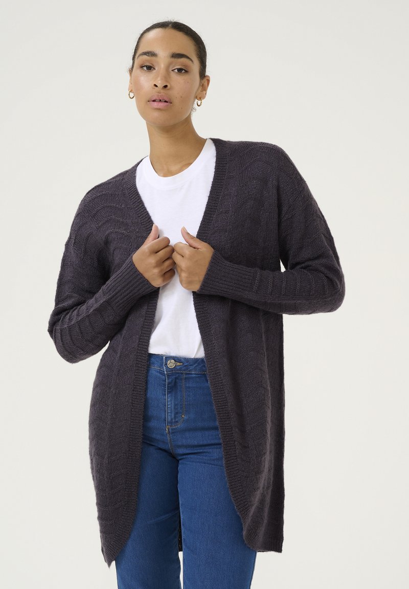 Cardigan lavorato a maglia grigio scuro con maniche lunghe, apertura frontale, motivo testurizzato e polsini a costine, abbinato a una camicia bianca e jeans blu.