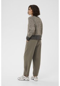 Maglione lavorato a maglia in beige e grigio con motivi testurizzati e polsini a costina, abbinato a pantaloni larghi verde oliva e scarpe da ginnastica leggere.