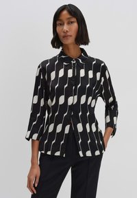 Camicia bianca e nera con un motivo ondulato, maniche lunghe, colletto a punta e chiusura con bottoni sul davanti. Tessuto di trama liscia.