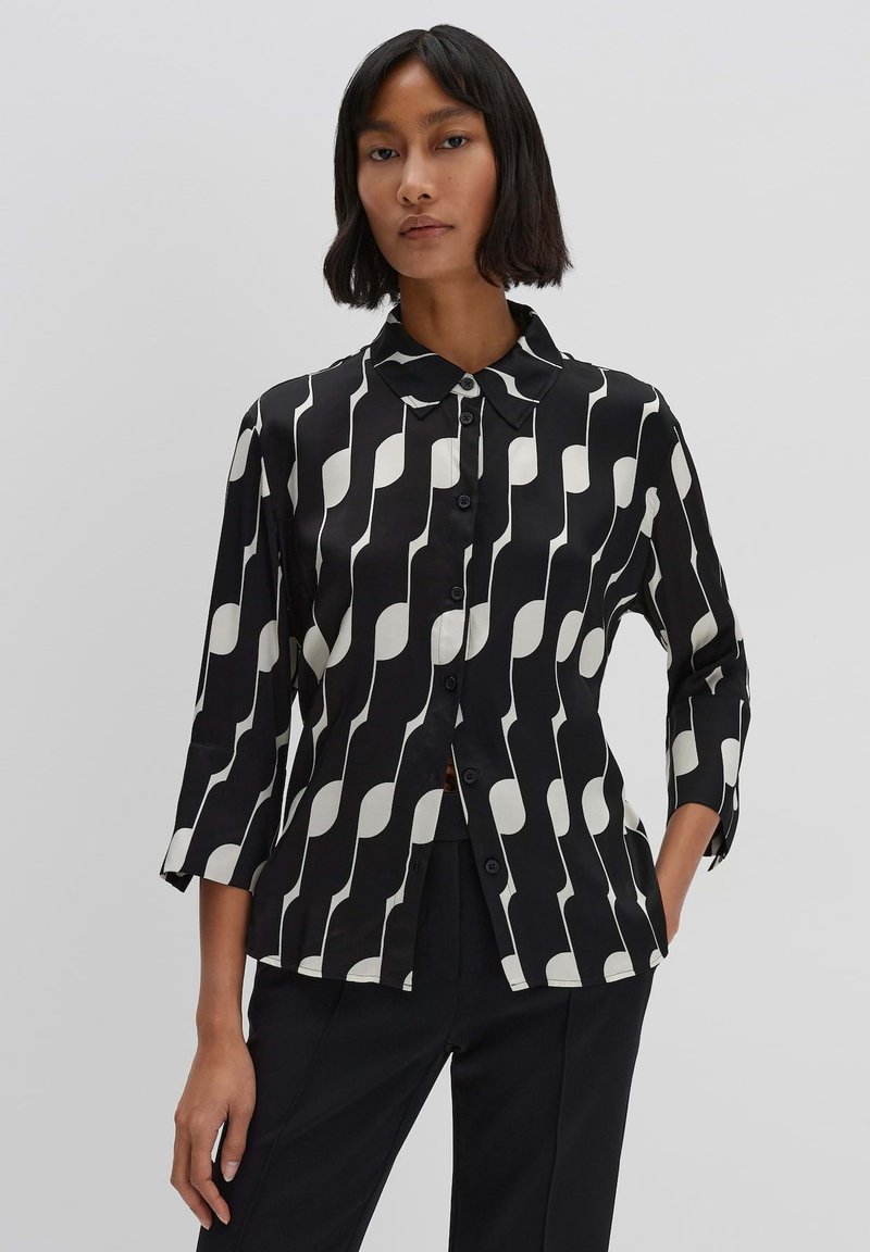Camicia bianca e nera con un motivo ondulato, maniche lunghe, colletto a punta e chiusura con bottoni sul davanti. Tessuto di trama liscia.