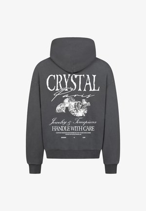 Šedá mikina s kapucí se velkým bílým grafickým motivem na zadní straně, který obsahuje nápis "CRYSTAL Paris", diamanty a pokyny k údržbě v kurzívě a tučném písmu.