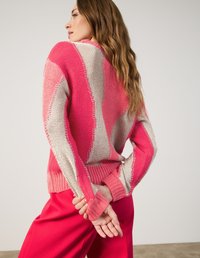 Gestreifte Strickjacke in Pink und Weiß mit strukturierter Oberfläche, langärmlig und mit gerippten Bündchen, kombiniert mit pinken Hosen.
