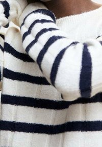 Biały sweter z granatowymi poziomymi paskami. Miękki, teksturowany materiał z okrągłym dekoltem i ribbowymi mankietami. Widoczne detale wzoru dzianiny.