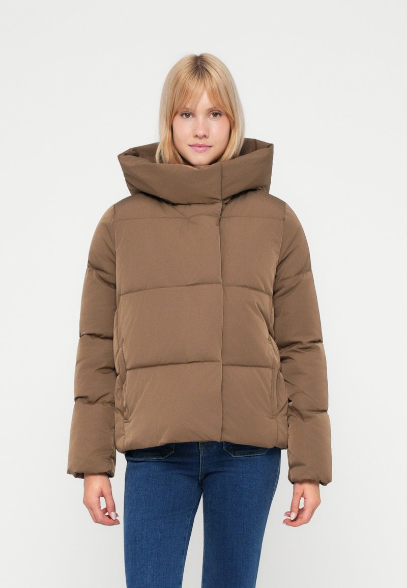 Casaco puffer castanho com gola alta, padrão acolchoado e mangas longas. Usado sobre um conjunto de ganga azul. Textura de tecido suave.