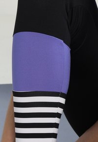 Czarne i fioletowe legginsy sportowe z paskowanym dolnym odcinkiem w czerni i bieli, wykonane z gładkiego i elastycznego materiału.