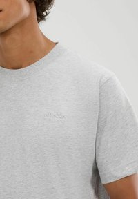 Graues Baumwoll-T-Shirt mit geripptem Rundhalsausschnitt, kurzen Ärmeln und dezent geprägtem Logo auf der Brust. Weicher Stoff, lässige Passform.