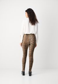 Leggings z vzorcem leopardjeve kože iz raztegljivega materiala, prilegajoča se zasnova, v kombinaciji z belim topom z dolgimi rokavi. Črne robustne čevlje dopolnjujejo videz.