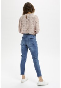 Ljusrosa spetsblus med ett nyckelhål bak, kombinerad med mediumtvättade denimjeans med två bakfickor och design med avsmalnande ben.